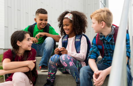 Pre-teens on steps outside school, wearing bright clothes and backpacks. They're facing each other and smiling and laughing