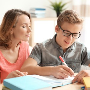 Parent at home with kid helping them with homework. Kid has short blonde hair and is wearin glasses.