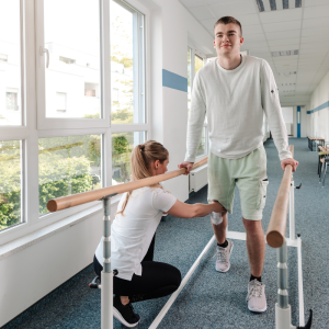 Teen using support bars and working with a physical therapist to practice walking and streghtening