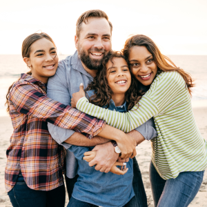 Family (two parents and two kids) smiling on a beach, hugging